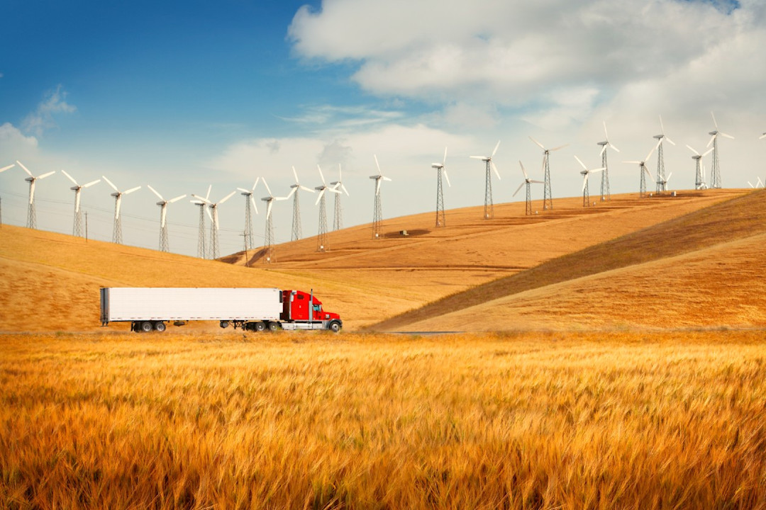 A US truck drives through a corn field with wind turbines visible in the background.jpg